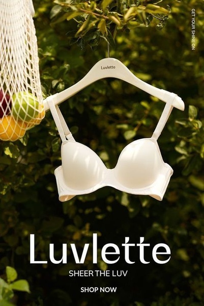 A clean, outdoor product shot of a white bra hanging on a hanger against a blurred, lush green background, emphasizing a fresh, natural aesthetic.